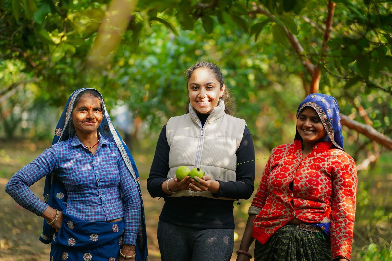 Three women posing in a sunlit guava orchard